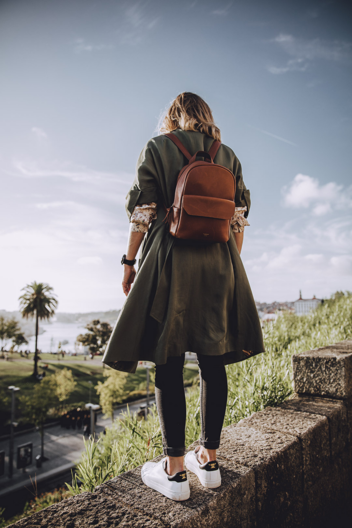 Frau mit kleinem braunen Leder-Rucksack, dunkelgrünem Cardigan und weissen Sneakers