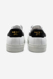 Weisser Unisex-Sneaker von hinten mit schwarzem Detail und goldenem Amboss in der Fersenpartie