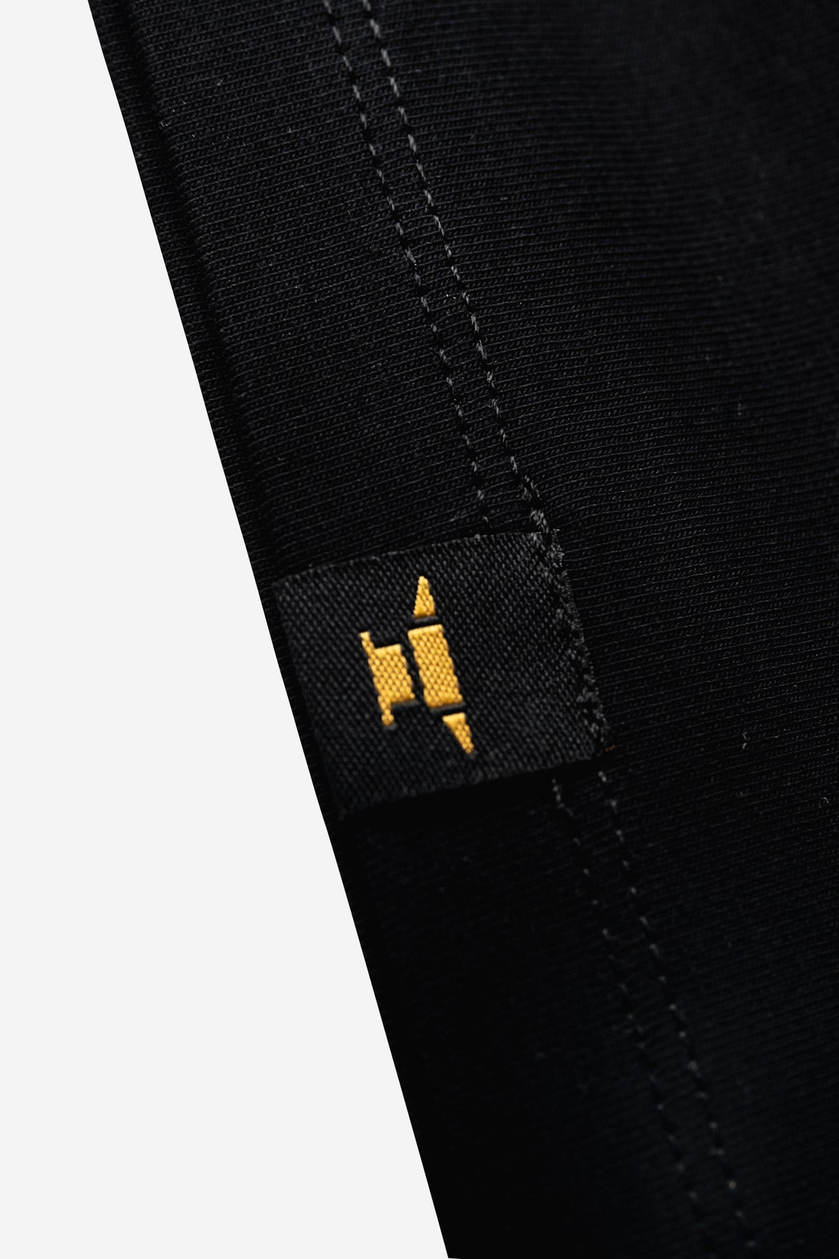 Schwarzes, talliertes Baumwoll T-Shirt für Damen mit kleinem, goldenen DIE SCHMIEDE Amboss-Logo am Saum unten